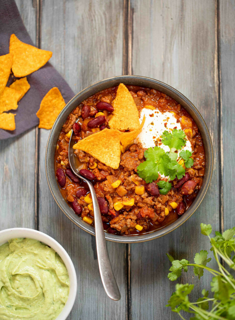 Un bol avec chili con carne avec nachos et coriandre dessus